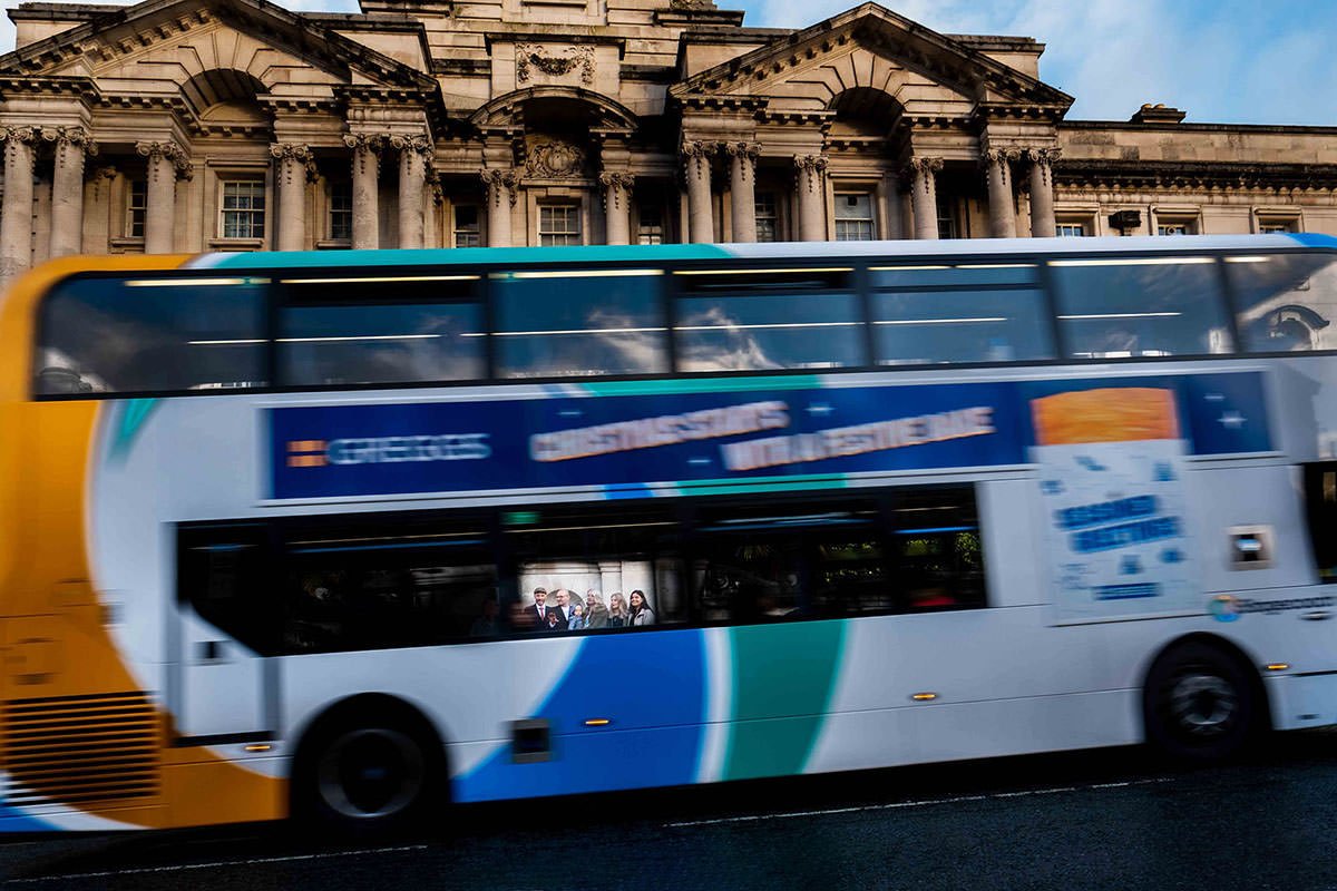 Group portrait through the window of a moving bus outside Stockport Town Hall