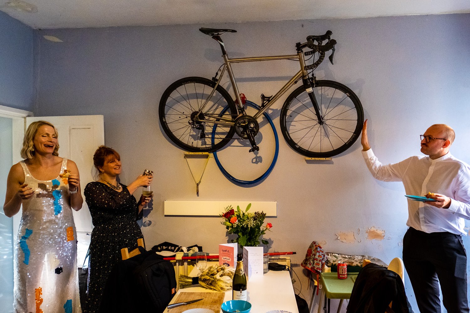 Groom touches his bike as his bride and a guest look on