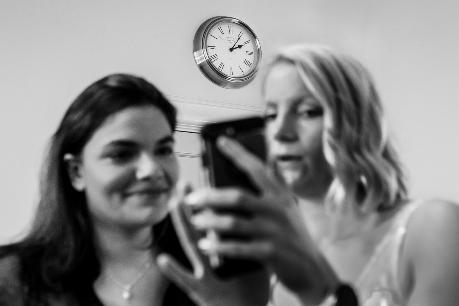 Bride and her sister look at a phone as the clock ticks past 2pm