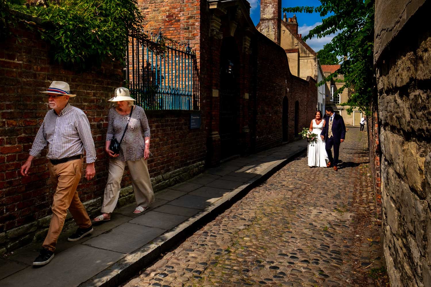 Bride and groom walk down cobbled street near York Minster behind two people