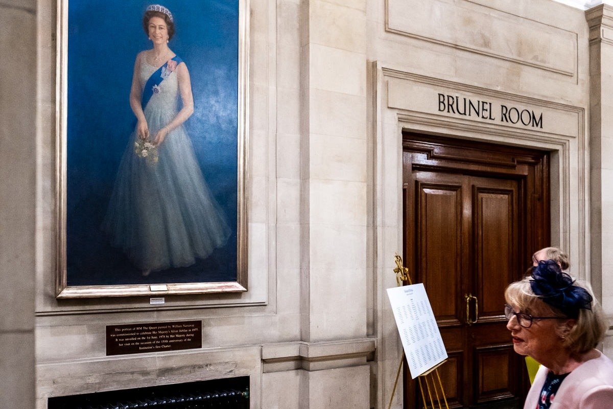 Mother of groom enters ceremony room, with painting of Queen in background