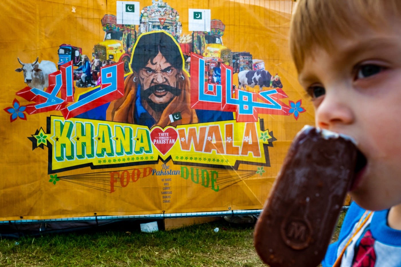 Child eats ice cream in front of a poster at Camp Bestival