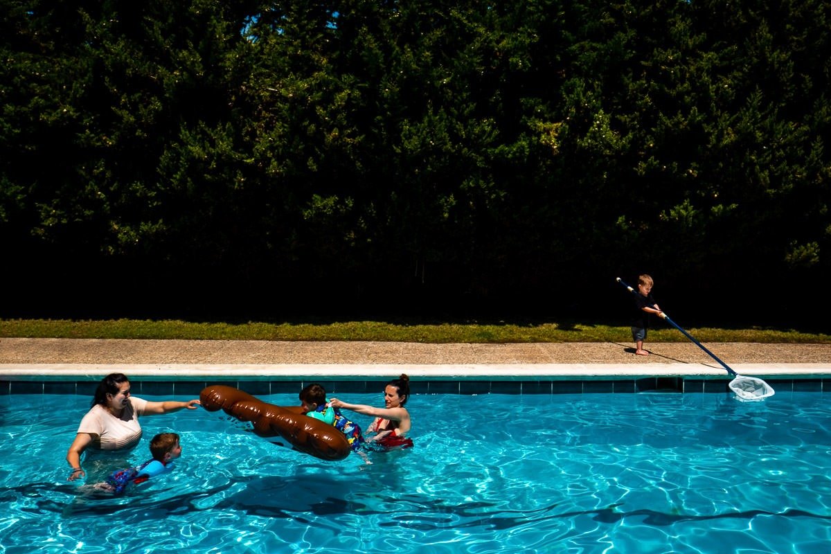 People play in swimming pool as child cleans it with a giant net