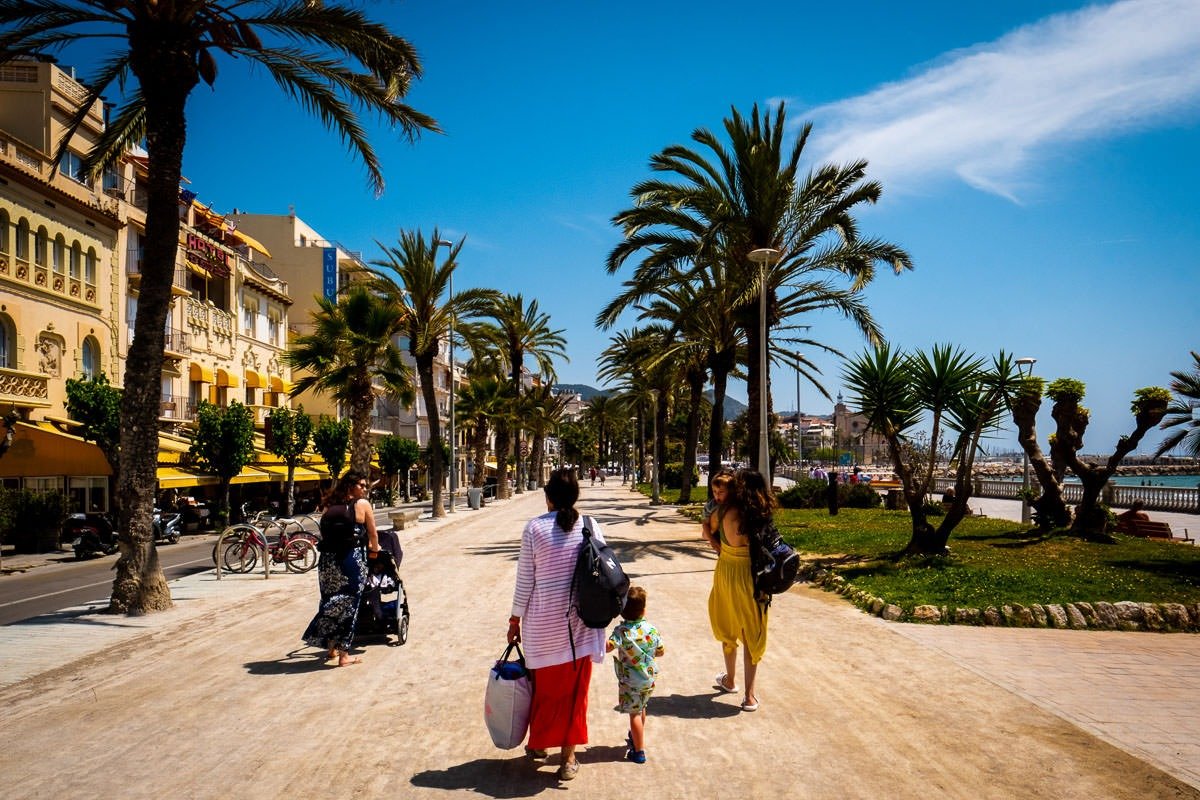 Adults and children walk along promenade in Sitges, Spain