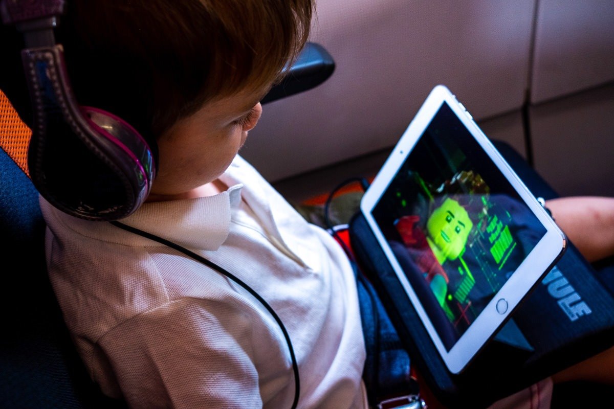 Child wearing headphones watches iPad during plane journey