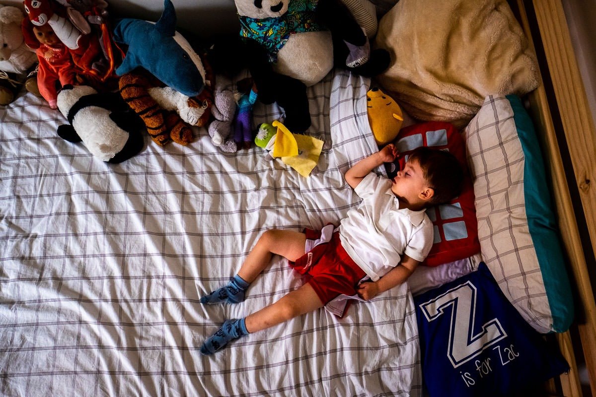 Child sleeps on bed surrounded by cuddly toys