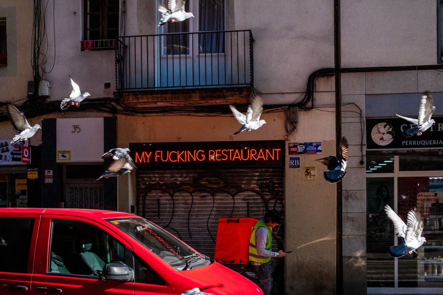 Pigeons fly past a restuarant called 'My Fucking Restaurant'