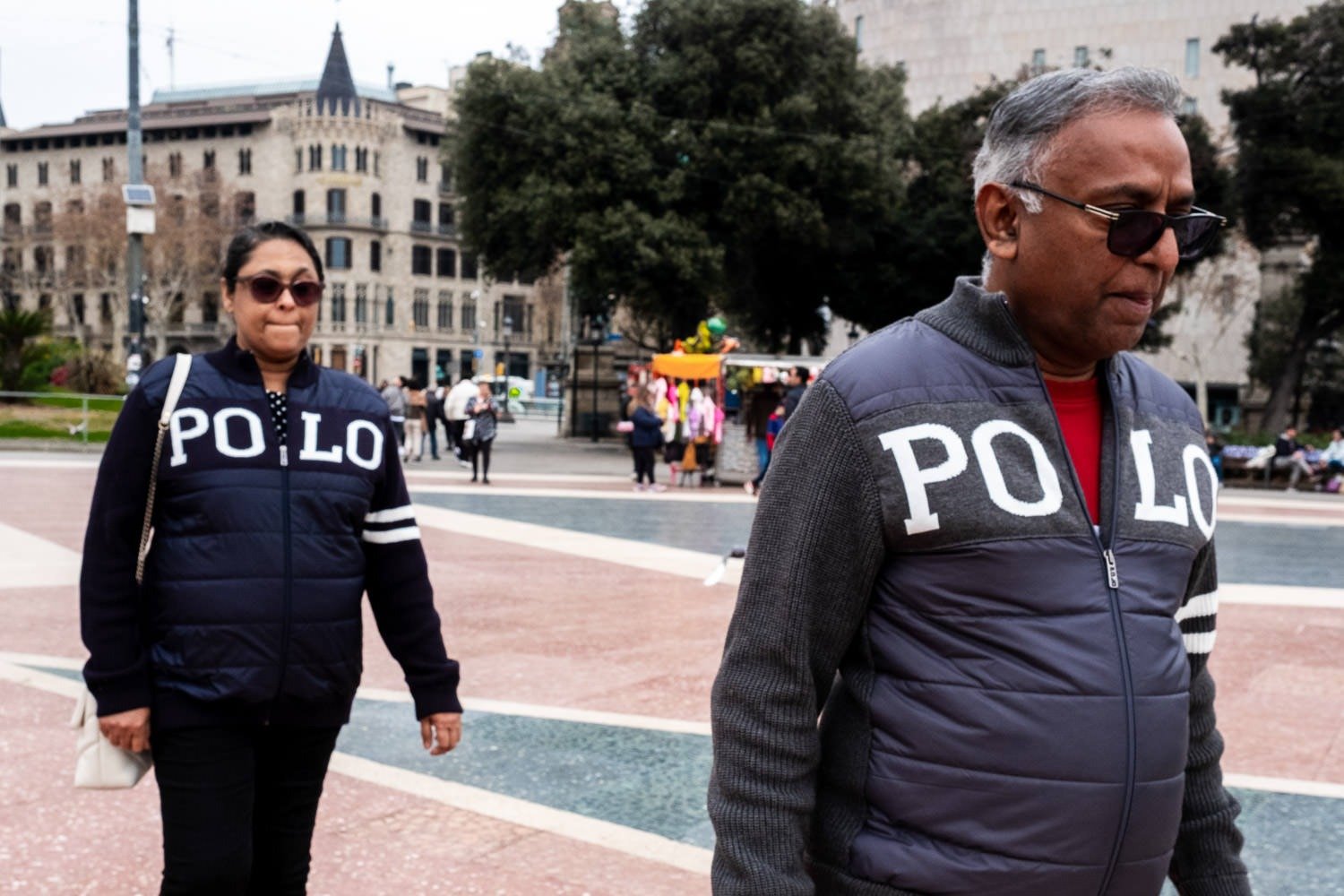 Man and woman in matching jackets walk through Placa Catalunya in Barcelona