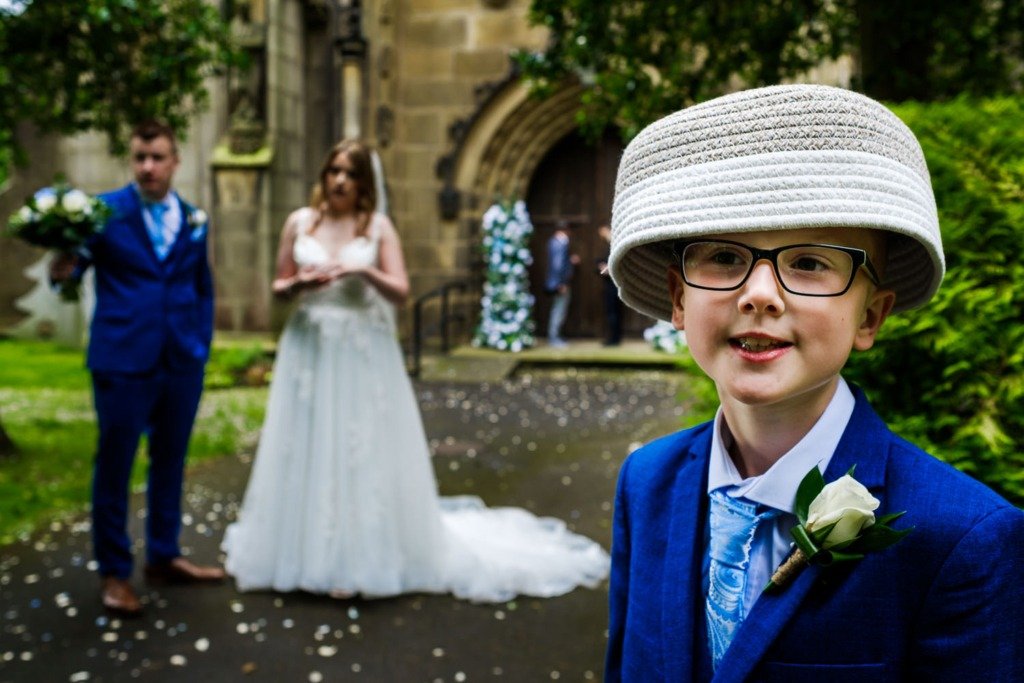 A child uses a flower basket as a hat as the bride and groom stand in the background after being married at Pleasington Priory in Lancashire