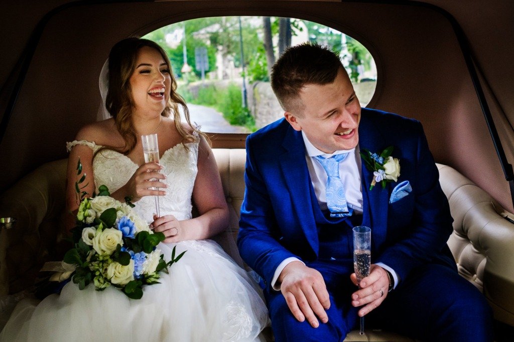 Bride and groom laugh in the back of a classic car at Pleasington Priory before driving to Mytton Fold Hotel to celebrate their wedding