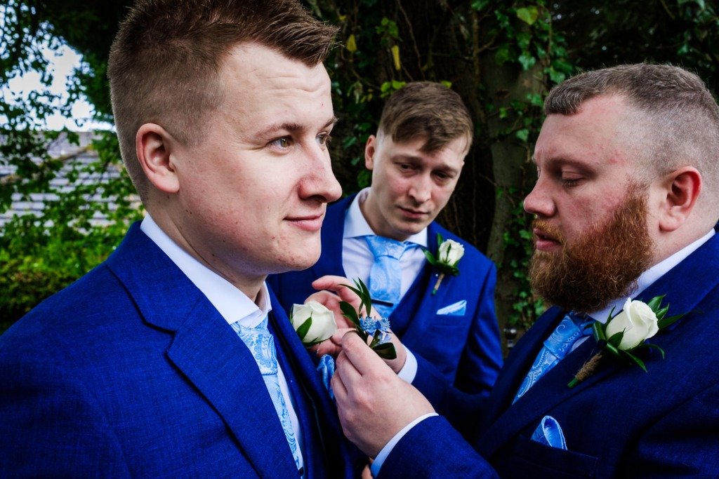 The groom has his button hole corrected by a groomsman as the best man looks on beforea Mytton Fold wedding