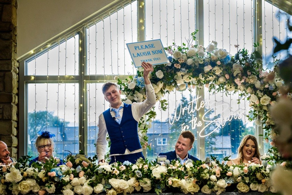 The best man holds up a sign saying 'Please laugh now' during speeches at a Mytton Fold wedding in the Ribble Valley