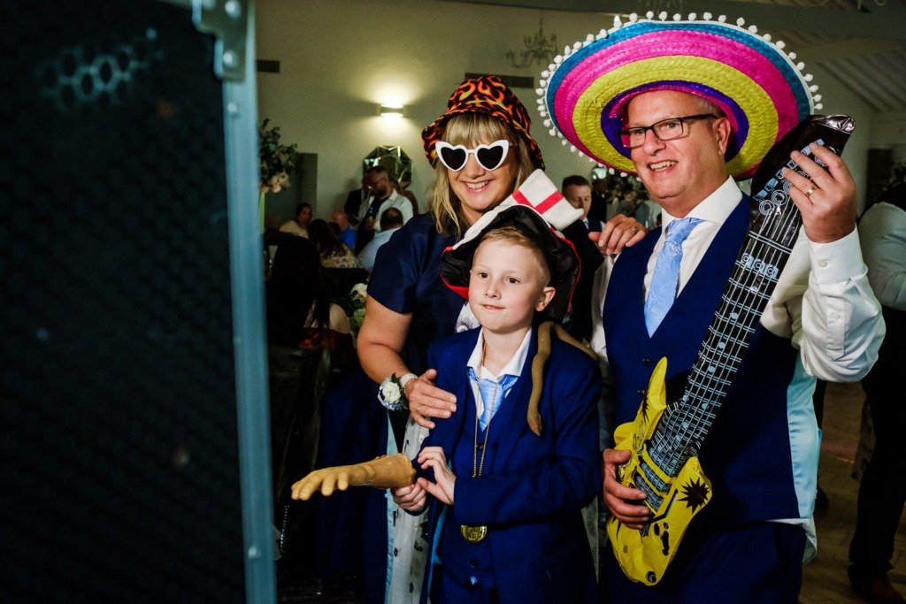 Guests in fancy dress play blow-up instruments in front of a photo booth at a Mytton Fold wedding