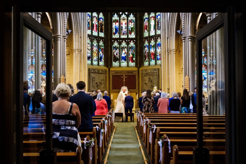 Bride and groom stand in the aisle at Pleasington Priory before celebrating their wedding at Mytton Fold Hotel