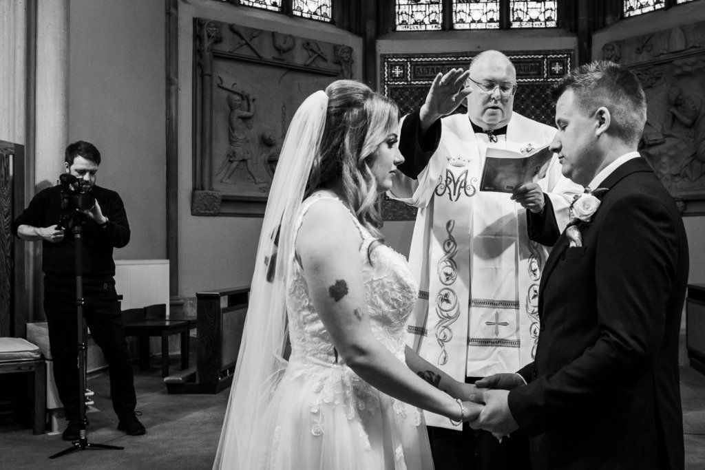 A videographer films the bride and groom during their Mytton Fold wedding service at Pleasington Priory in Lancashire